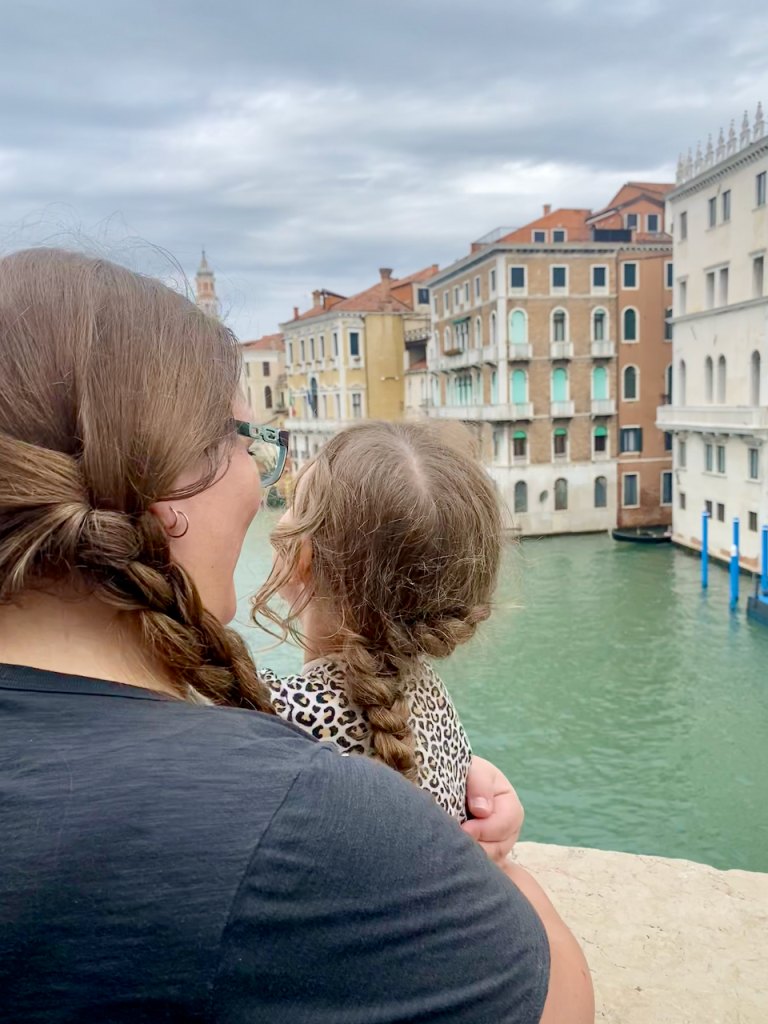Emily and her daughter standing together on the Rialto Bridge in Venice, facing away as they overlook the Grand Canal—capturing a quiet family travel moment of connection and discovery.
